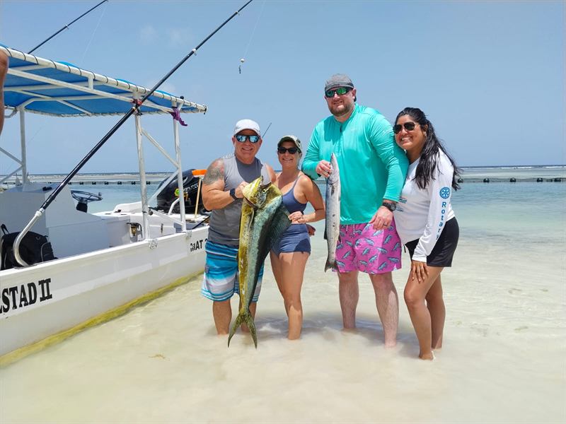 Pescadores en la orilla mostrando un dorado y una barracuda junto a la lancha