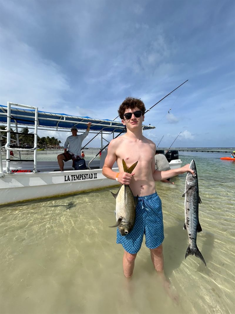 Pescador mostrando un jurel y una barracuda frente a la lancha La Tempestad II
