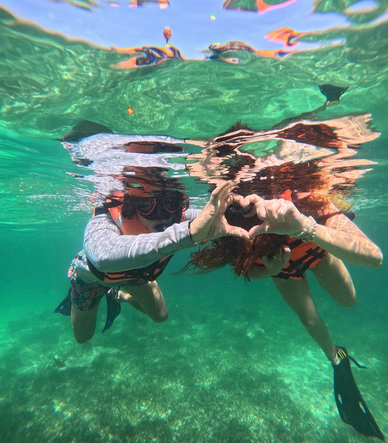 Dos personas haciendo un corazón con las manos mientras hacen snorkel en Mahahual